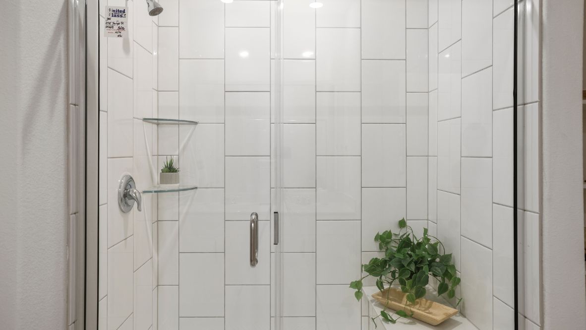 Modern primary bathroom with double vanities, granite countertops, and a glass-enclosed shower with a walk-in closet.