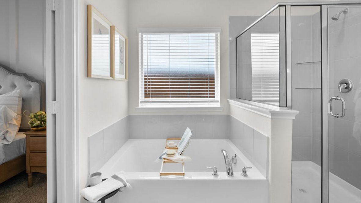 Bright white primary bathroom bathtub with large window and lo