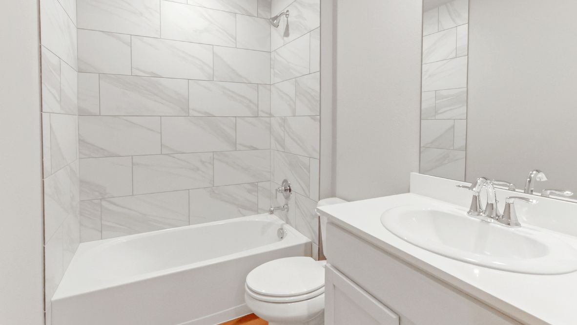 Modern secondary bathroom showcasing white cabinets, a sink, quartz countertops, and a 12x24 tiled shower surround.