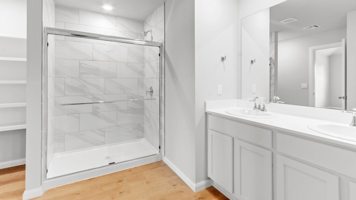 Modern primary bathroom with double vanities, quartz countertops, and a glass-enclosed shower with a walk-in closet.