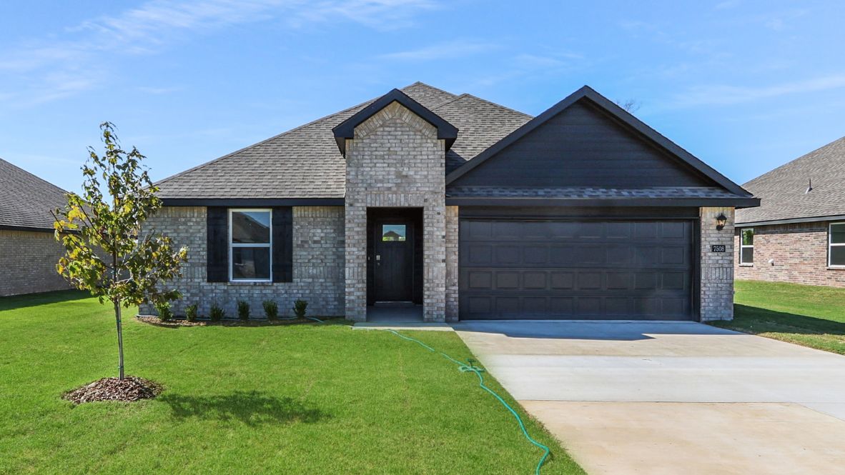 Newly built single story brick home with modern architecture, a double garage, and landscaped front yard.