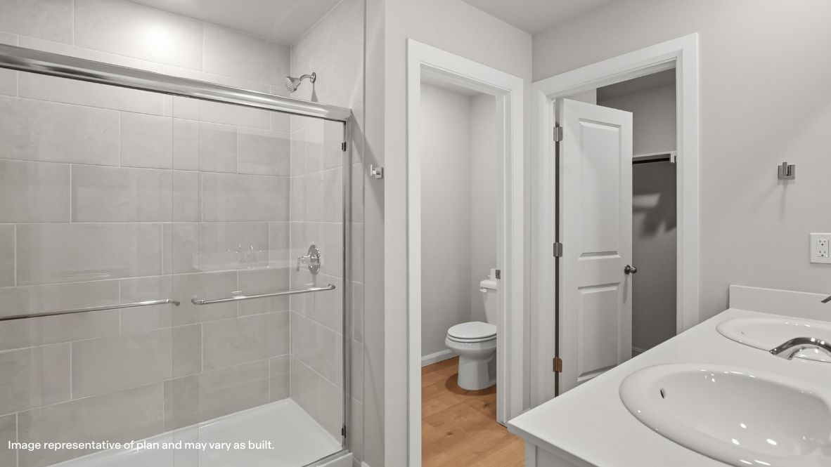 Modern primary bathroom with double vanities, quartz countertops, and a glass-enclosed shower with a walk-in closet