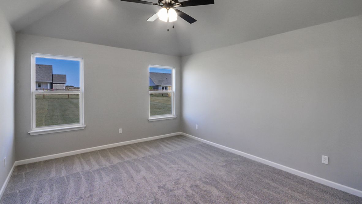 Primary bedroom with ceiling fan, plush carpeting, and a large walk-in closet.