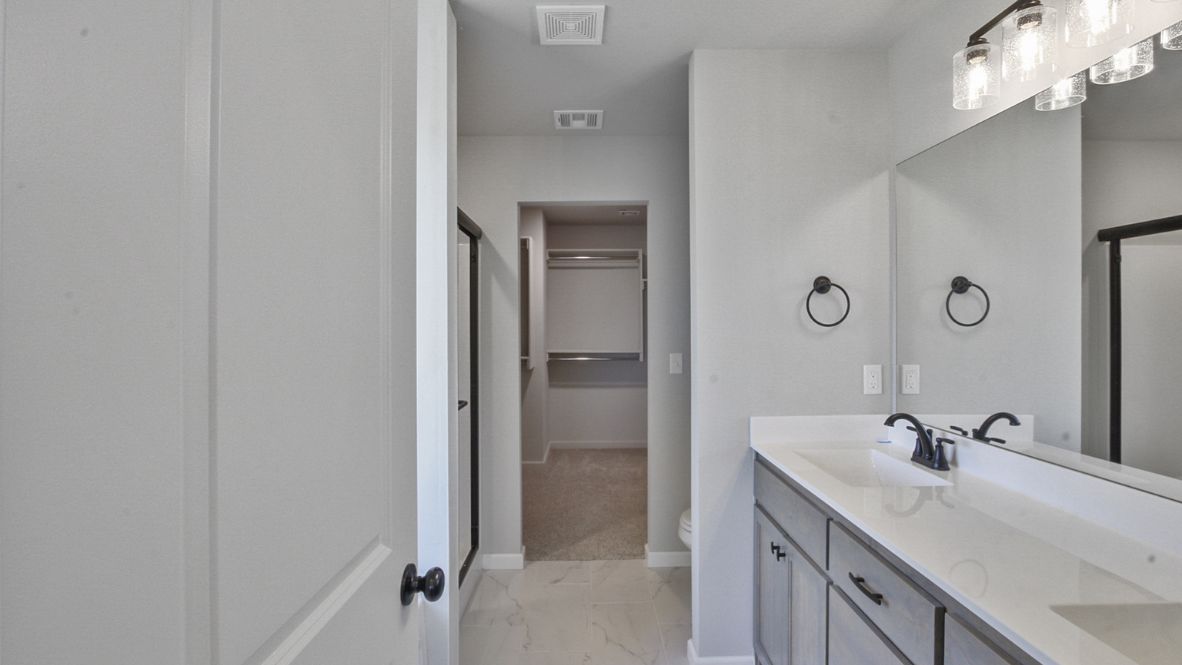 Modern primary bathroom with double vanities, granite countertops, and a glass-enclosed shower with a walk-in closet.