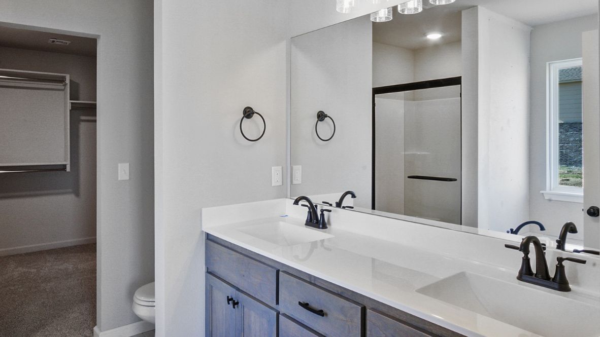 Modern primary bathroom with double vanities, granite countertops, and a glass-enclosed shower with a walk-in closet.