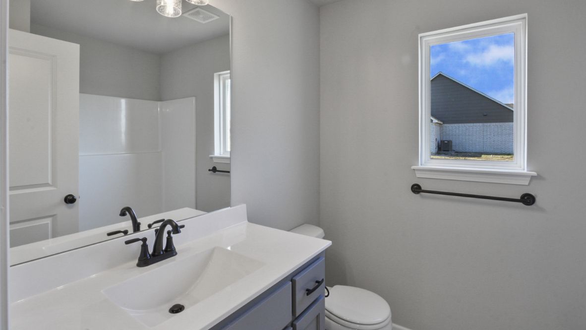Modern secondary bathroom showcasing white cabinets, a sink, quartz countertops, and a 12x24 tiled shower surround.