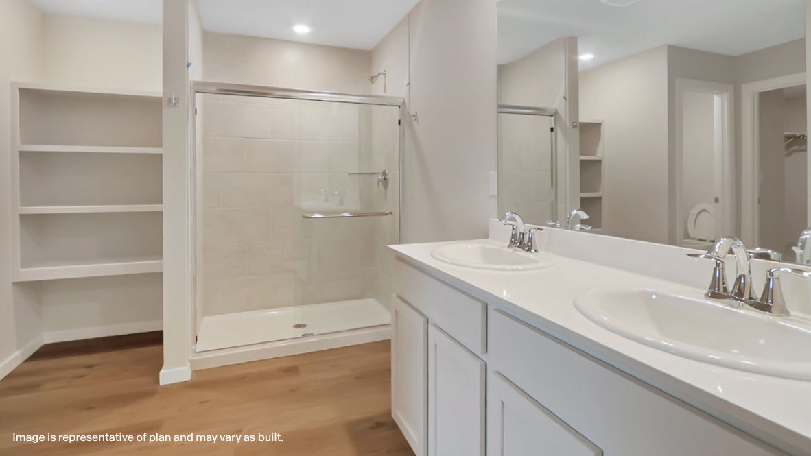 Modern primary bathroom with double vanities, quartz countertops, and a glass-enclosed shower with a walk-in closet.