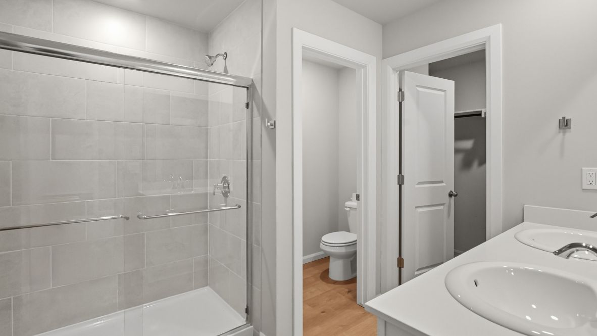 Modern primary bathroom with double vanities, quartz countertops, and a glass-enclosed shower with a walk-in closet.