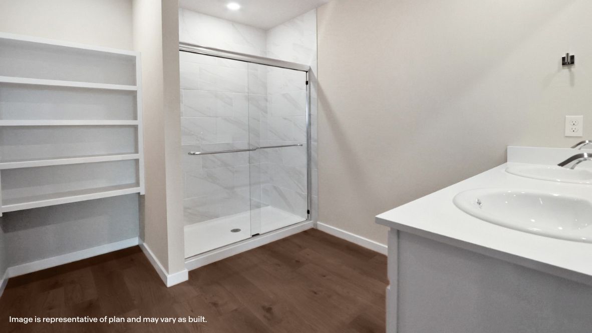 Modern primary bathroom with double vanities, quartz countertops, and a glass-enclosed shower with a walk-in closet.