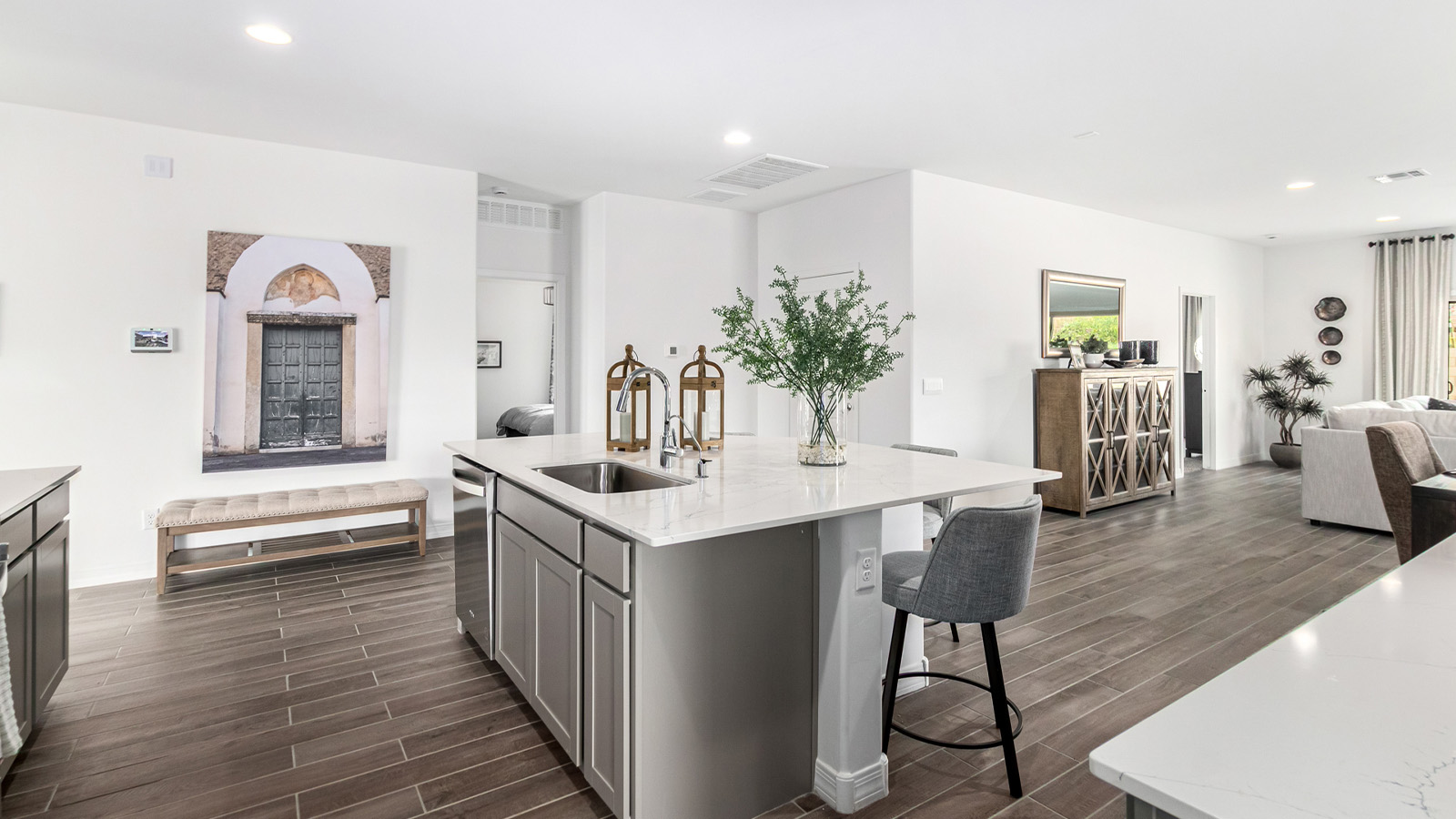 Step into The Kingston at Barnett Village, Marana, Arizona – a perfect blend of comfort, modern living, and energy efficiency. This thoughtfully crafted one-story home spans 2,068 square feet and offers four bedrooms and two bathrooms, ideal for families of all sizes.  The open-concept design features a spacious great room that effortlessly connects with the kitchen and dining area, creating an inviting central hub for everyday living and entertaining. The kitchen is equipped with contemporary appliances and a pantry, offering ample storage and convenience for meal preparation.  The primary bedroom, located at the rear of the home, provides a peaceful retreat with a private ensuite bathroom and a generous walk-in closet. The additional three bedrooms are positioned at the front of the house, offering versatility for use as guest rooms, a home office, or children’s bedrooms. Step outside to the covered patio, a perfect spot to enjoy the beautiful Arizona weather, whether for morning coffee or evening relaxation.  The Kingston also boasts a covered patio, perfect for enjoying Arizona’s beautiful desert evenings. Whether it’s morning coffee or evening relaxation, this outdoor space extends your living area into the serene landscape of Barnett Village.  Built with energy efficiency as a priority, the Kingston includes smart home technology, which not only simplifies daily living but also helps reduce utility costs. A two-car garage provides ample parking and additional storage space, enhancing the home’s functionality.